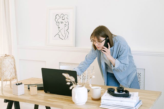 Person talking on the phone and looking at a laptop on a desk